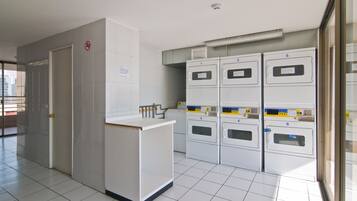 A laundry facility with multiple washing machines, a drying area, and a no-smoking sign on the wall.