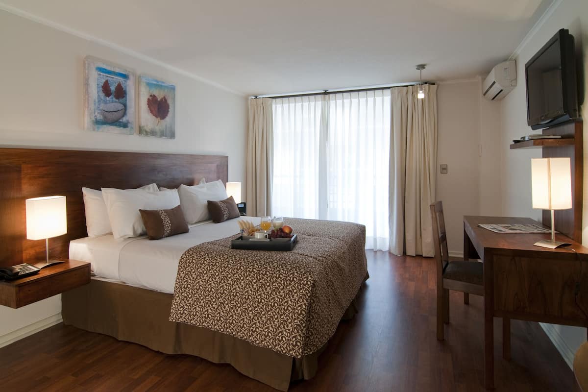 Ein Hotelzimmer mit einem großen Bett, Nachttischen, einem Schreibtisch und einem Fernseher.
