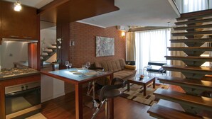 A modern kitchen with a built-in stove, dining area with a table and chairs, a sofa, and a staircase. - Park Plaza Apart Hotel (Santiago)