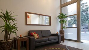 A modern living room with a sofa, a coffee table, two potted plants, a mirror, and a large window. - Park Plaza Apart Hotel (Santiago)