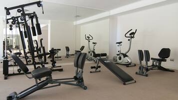 Ein modernes Fitnessstudio mit verschiedenen Trainingsgeräten, darunter eine Langhantelbank, Kurzhanteln und ein Laufband.