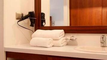 A bathroom with a wooden vanity, a mirror, a hairdryer, towels, and toilet paper.