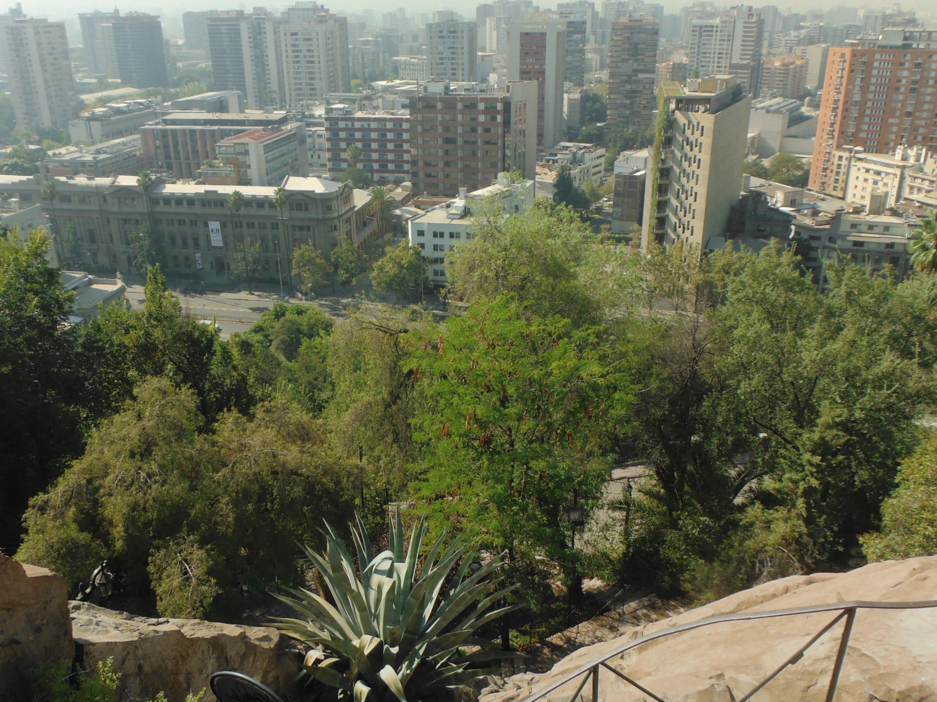 A cityscape with dense high-rise buildings, a central road, and surrounding greenery.