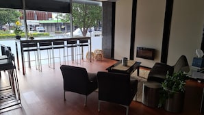 A modern living room with a TV, seating, and a view of the street through large windows.