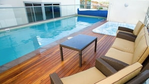 A poolside area with wooden flooring, a table, and two wicker lounge chairs.