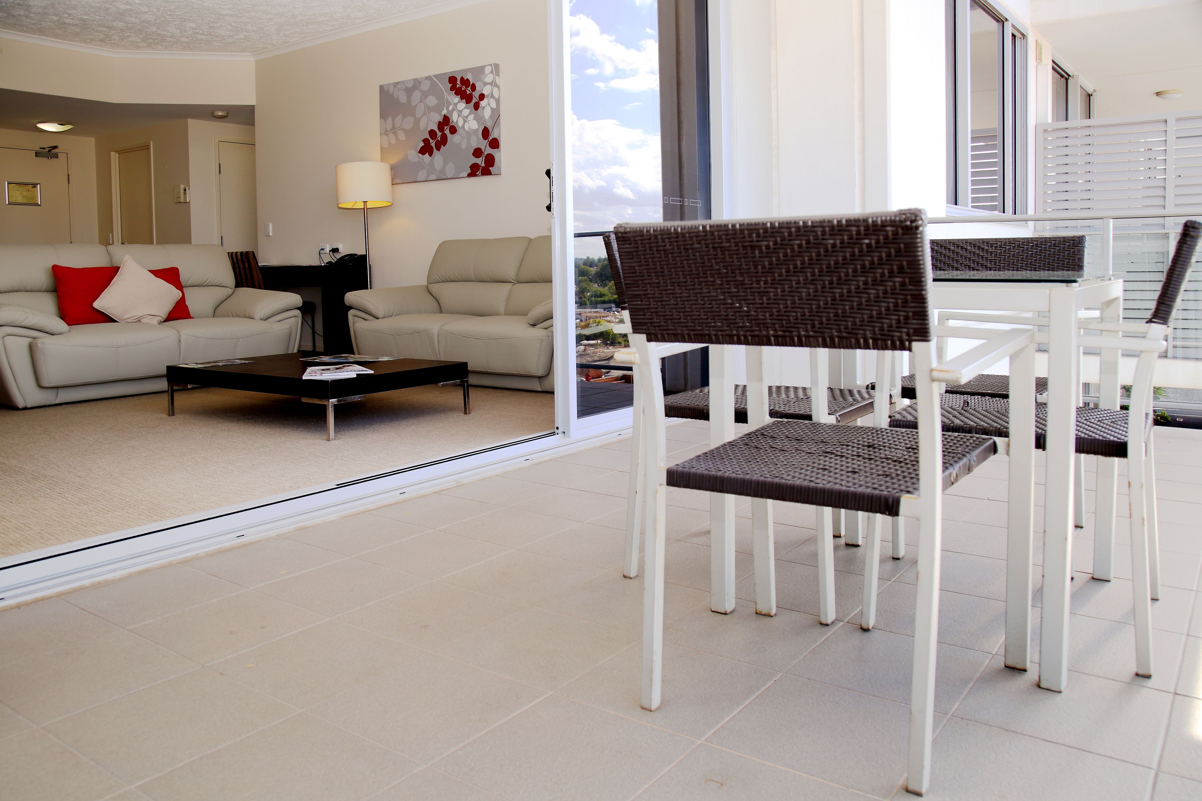 A modern living room with a sofa, coffee table, and a dining area with white chairs and a wicker table.