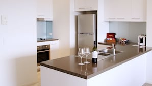 A modern kitchen with white cabinetry, a stainless steel refrigerator, and a central island with a sink and wine glasses.