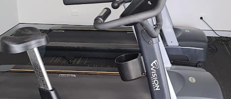 A stationary bike with a control panel and a display screen, placed in a room with a carpeted floor and a painting on the wall.