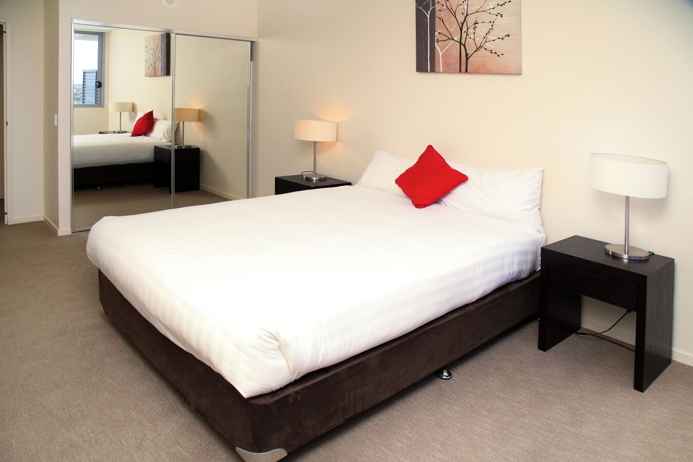 A hotel room with a large bed, a mirror, two bedside tables with lamps, and a painting on the wall.