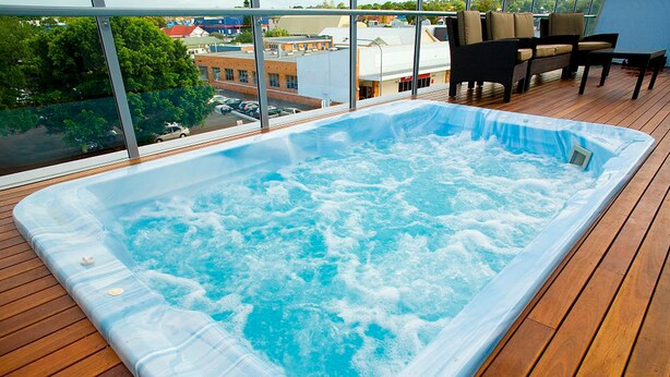 A hot tub on a wooden deck with a view of buildings and trees.