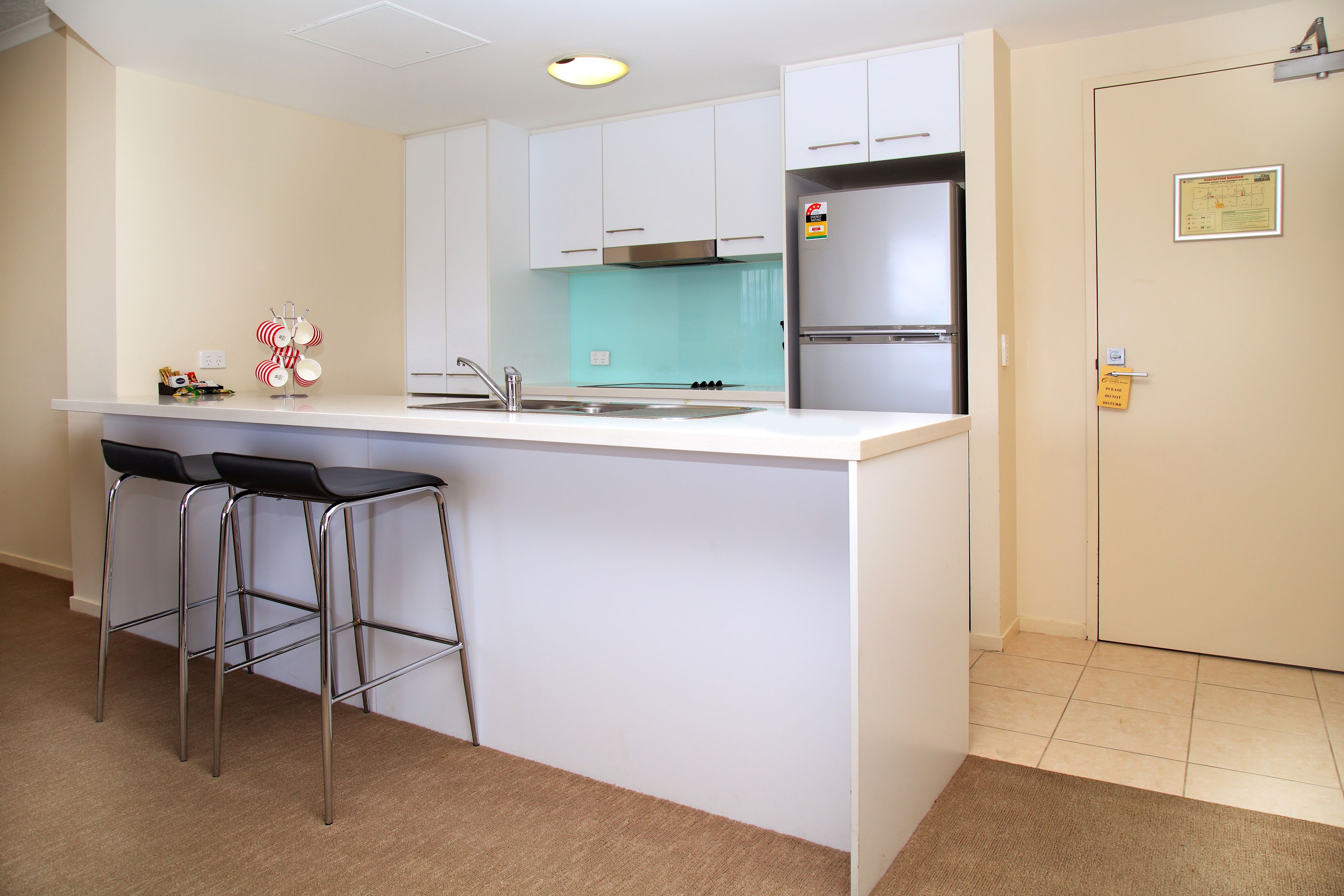 A modern kitchen with white cabinets, a stainless steel refrigerator, and a bar stool area.