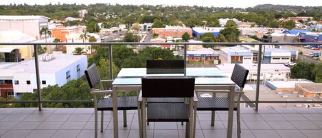 A balcony with a table and chairs, offering a view of a cityscape with buildings and greenery.