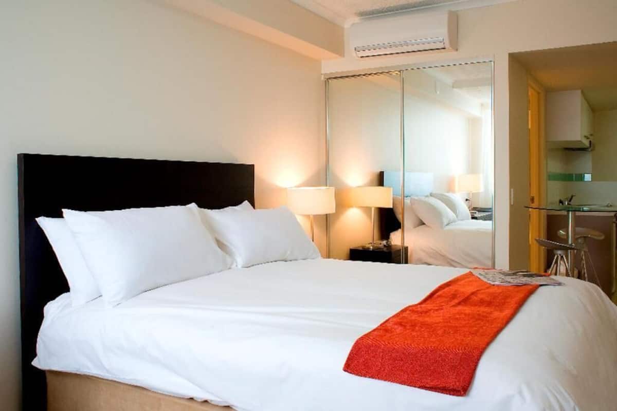 Ein Hotelzimmer mit einem großen Bett, einem Nachttisch, einem Spiegel und einer kleinen Küchenzeile.