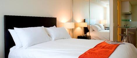 Ein Hotelzimmer mit einem großen Bett, einem Nachttisch, einem Spiegel und einer kleinen Küchenzeile.