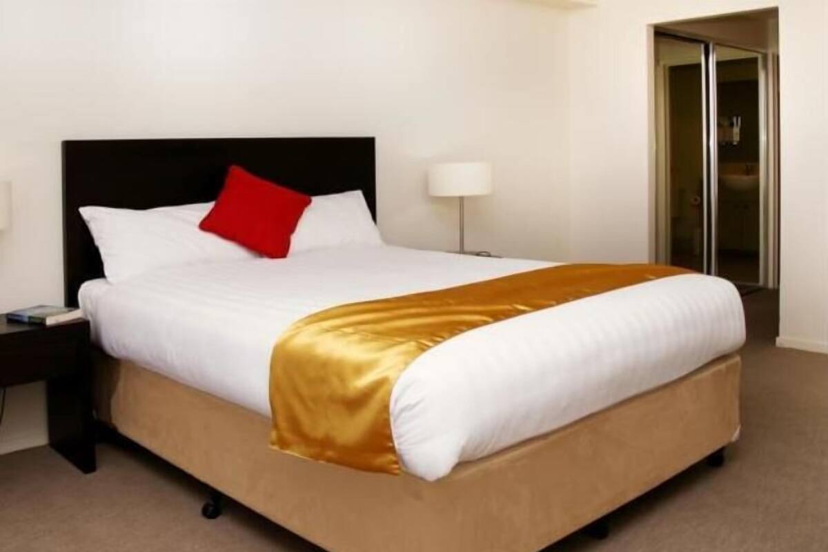 Ein Bett mit einer weißen Matratze, einem roten Kopfkissen und einer goldenen Decke.