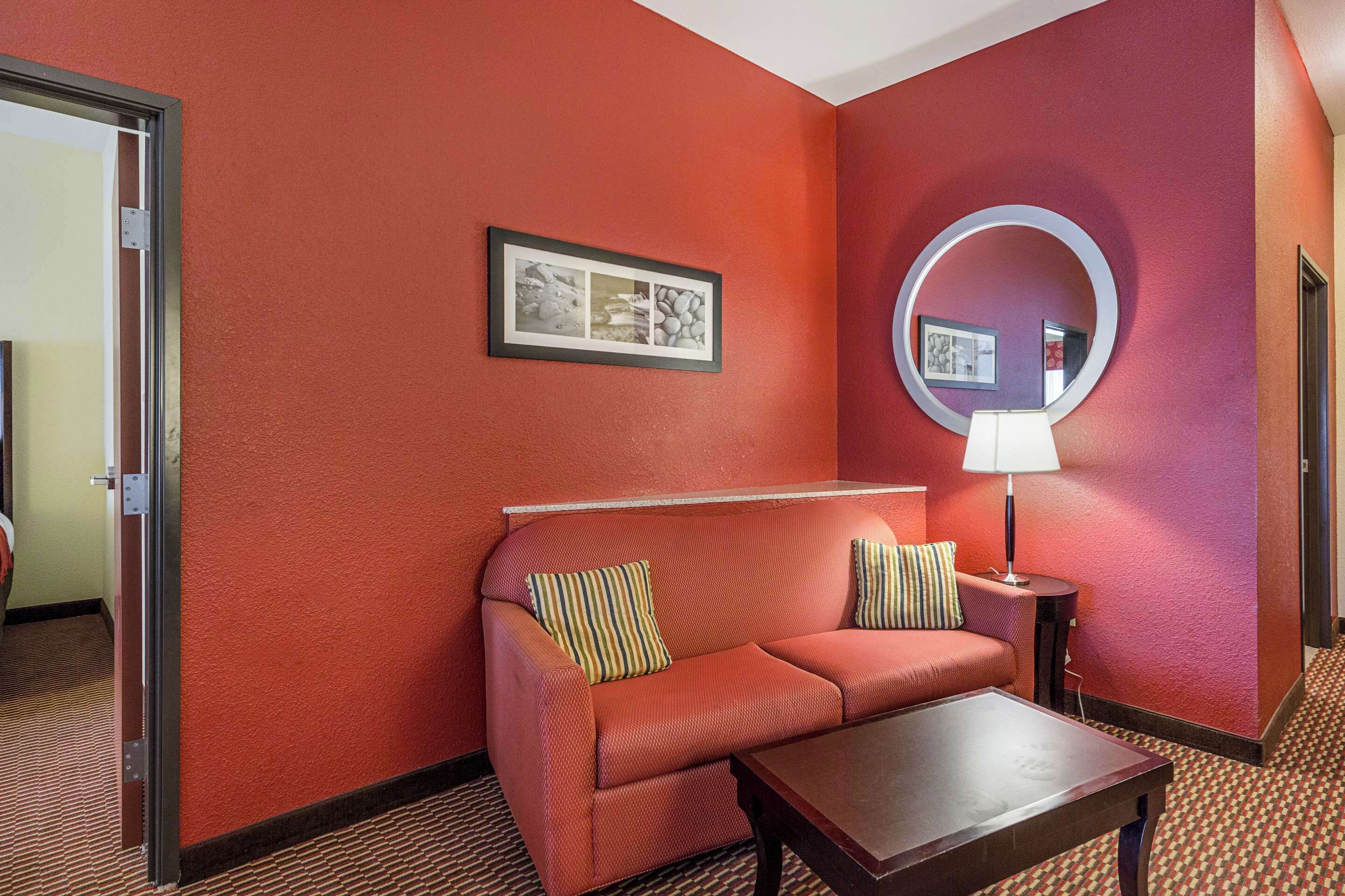 A hotel room with a red wall, a sofa with striped pillows, a round mirror, and a small table.