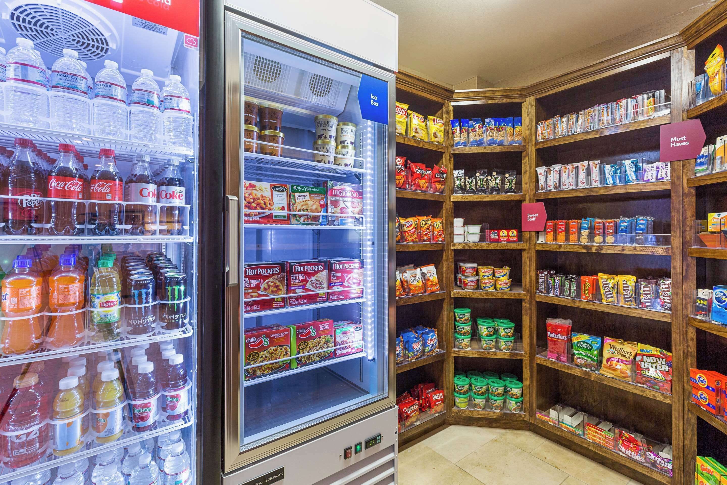 Um dispensador de bebidas refrigeradas e prateleiras repletas de lanches e alimentos.