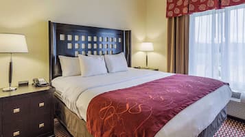 Hotellihuone, jossa on suuri sänky, tumma pääty, kaksi yöpöytää, joissa on lamput, puhelin ja kuviollinen verho.