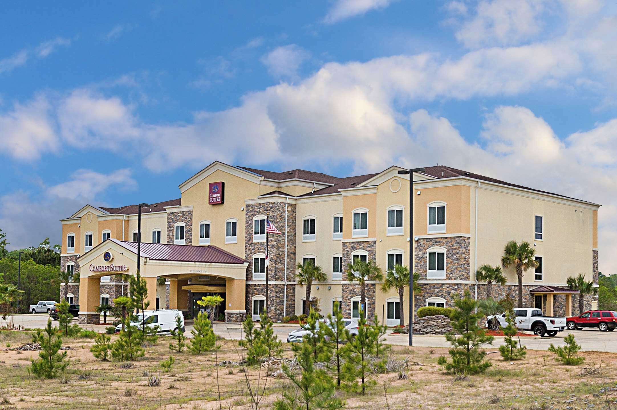A Comfort Suites hotel with a two-story structure, a covered entrance, and a parking lot with several vehicles.