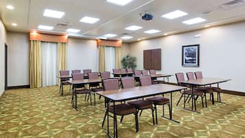 A conference room with tables and chairs, a projector, and a framed picture on the wall.