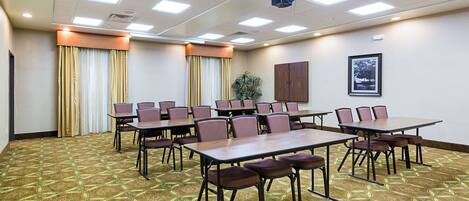 A conference room with tables and chairs, a projector, and a framed picture on the wall.
