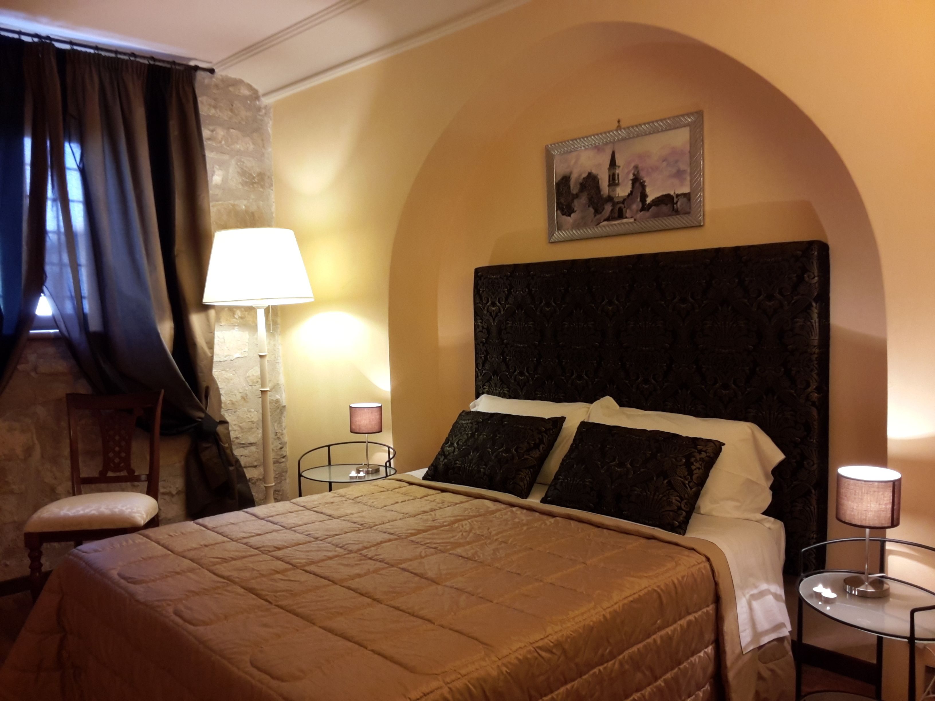 Une chambre d’hôtel avec un grand lit, une tête de lit, deux lampes de chevet, un tableau au mur et un mur en pierre.