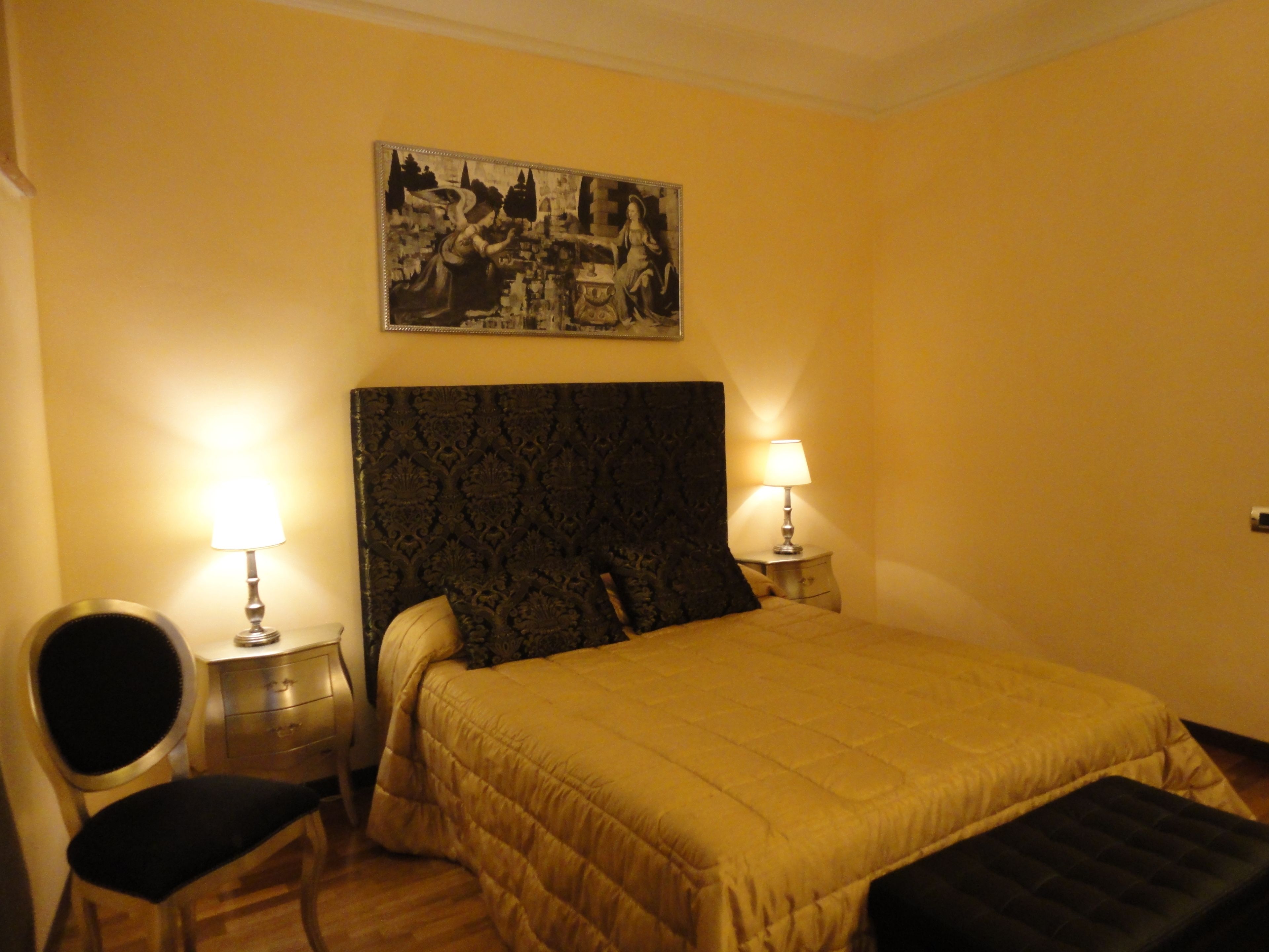 A hotel room with a large bed, two bedside tables with lamps, a chair, and a painting on the wall.