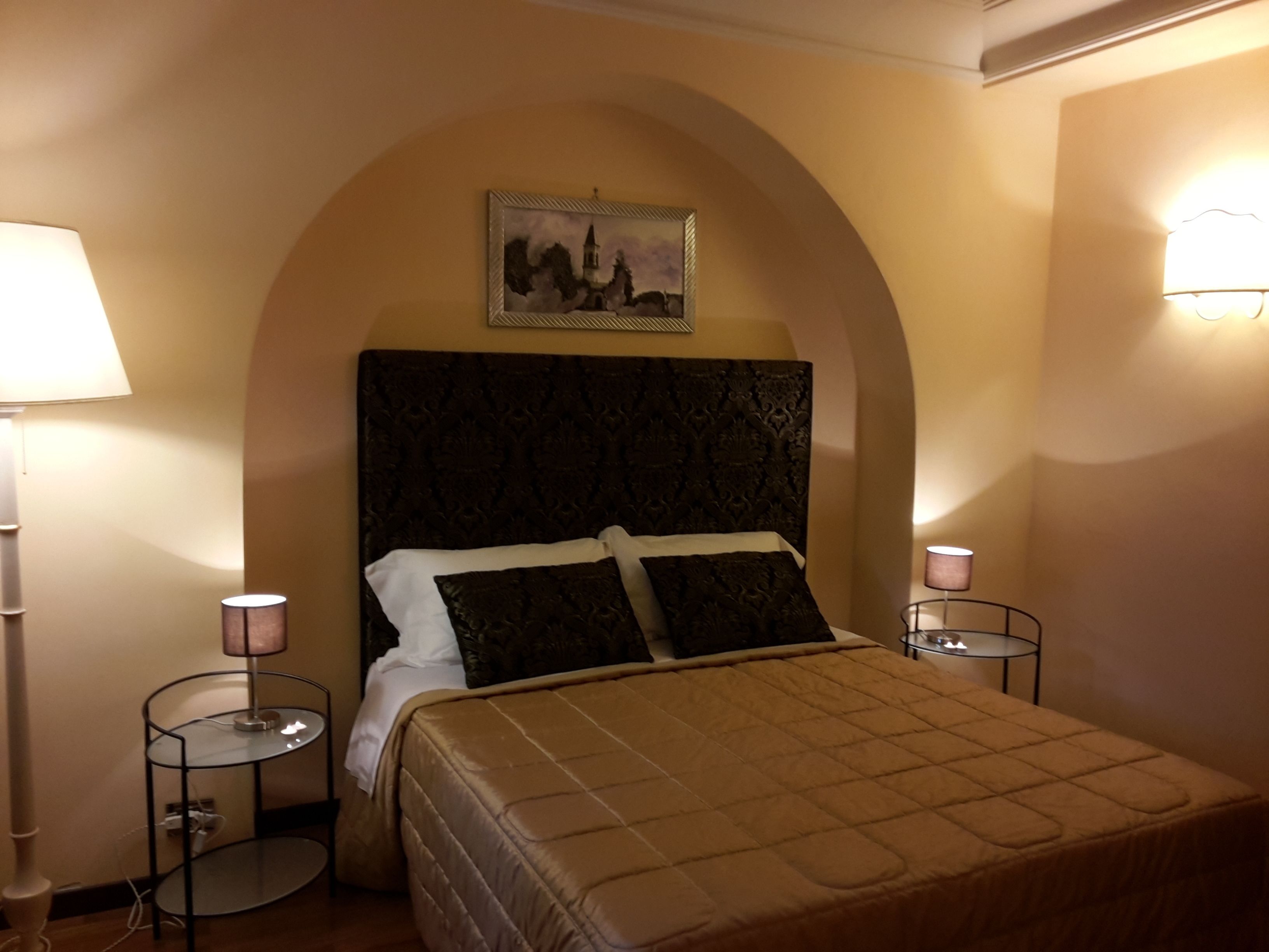 Ein Schlafzimmer mit einem großen Bett, zwei Nachttischen, einer Kopfteil und einem an der Wand hängenden Bild.