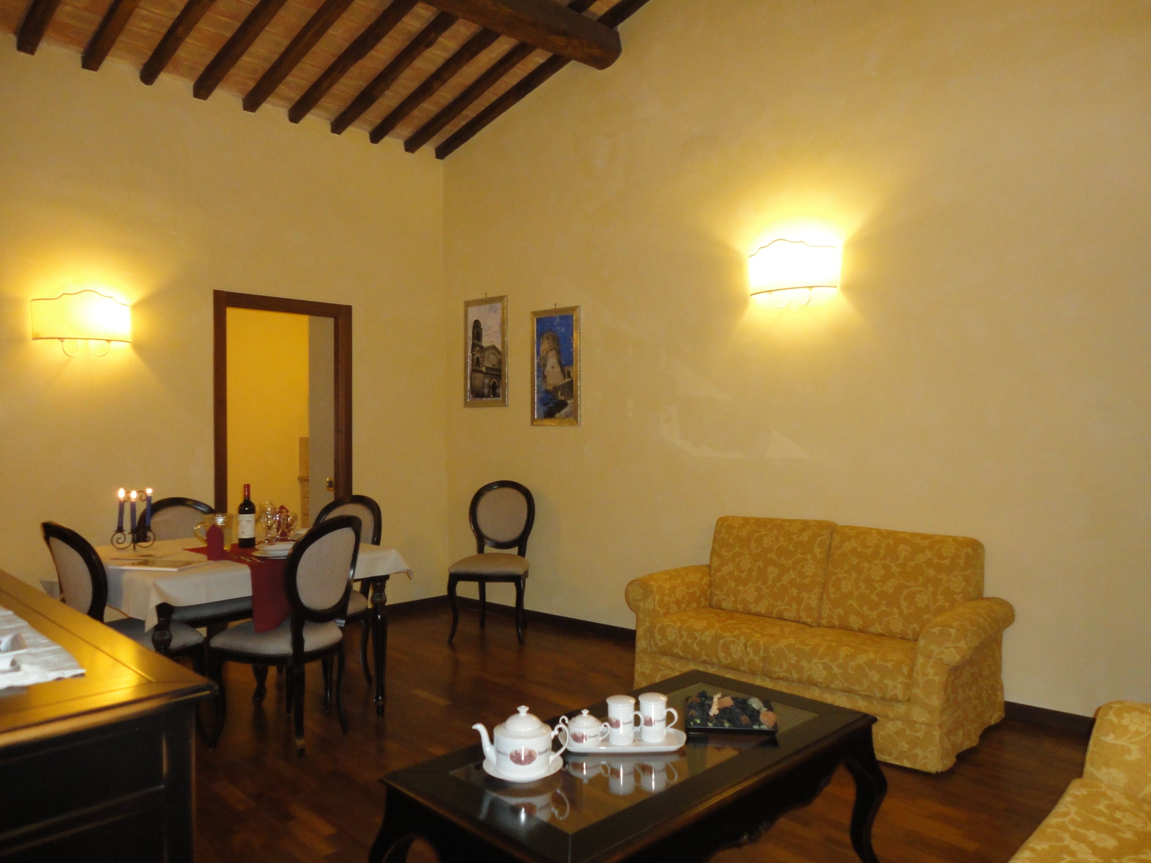 A living room with a sofa, a coffee table with tea set, a dining table with chairs, and wall-mounted lights.