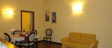 A living room with a sofa, a coffee table with tea set, a dining table with chairs, and wall-mounted lights.