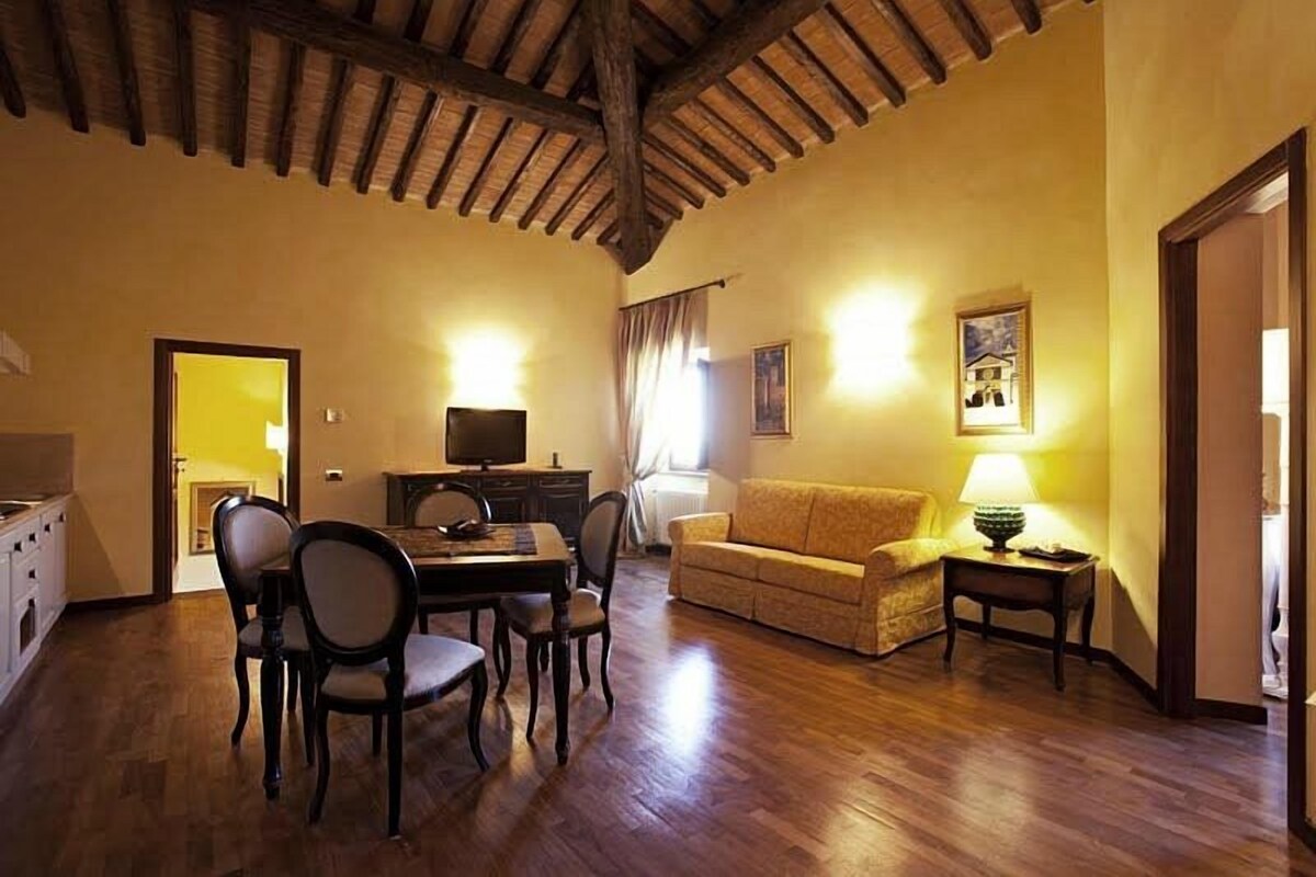 A cozy living room with a wooden ceiling, a dining table with chairs, a sofa, and a TV.