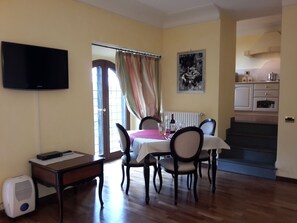 A dining area with a table set for four, a television mounted on the wall, and a kitchen in the background. - Castello Izzalini Todi Resort (Todi)