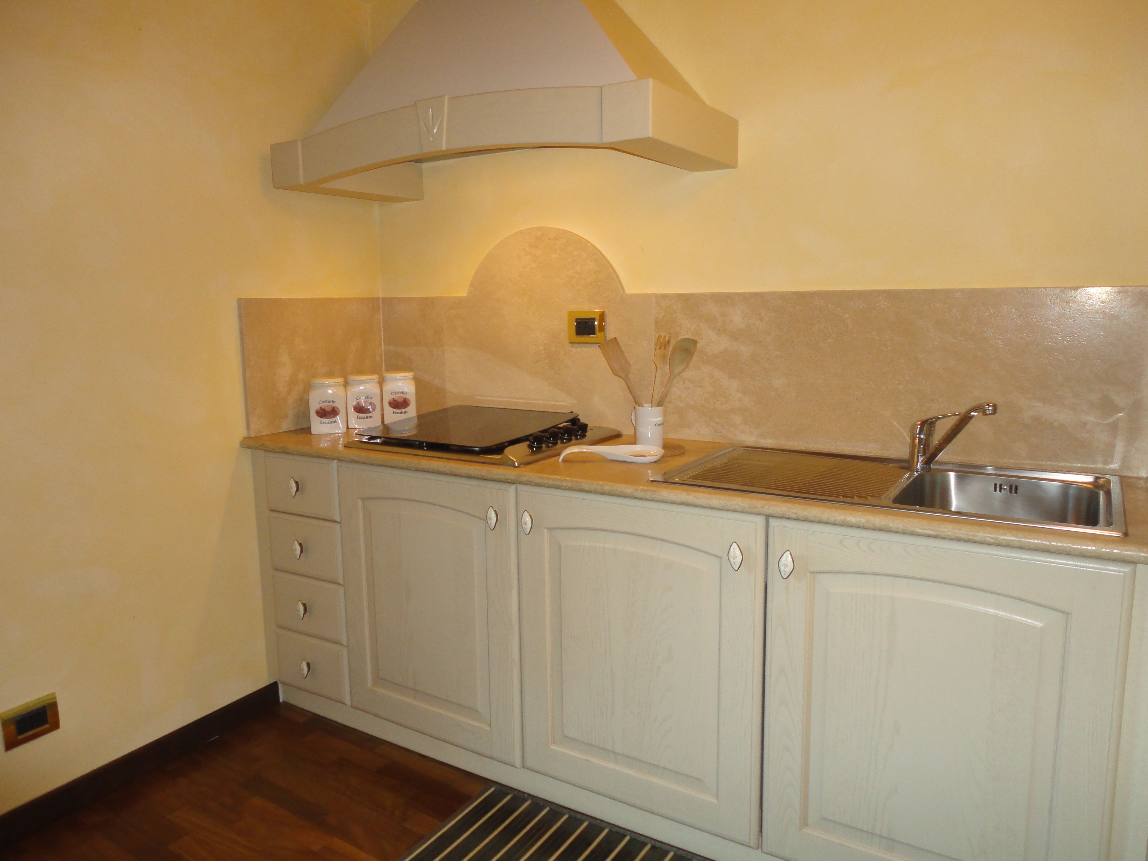 A kitchen with a stainless steel sink, a stove, and cabinets. There are three jars on the counter.