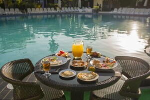 Mesa de jantar com itens de café da manhã e bebidas à beira da piscina.
