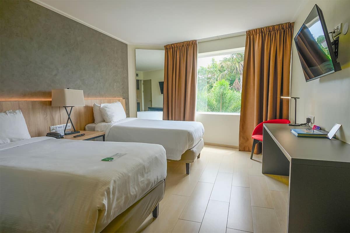 Una habitación de hotel con dos camas, un escritorio, un televisor y una ventana con cortinas.