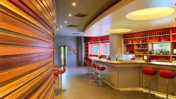 A bar area with a curved wooden wall, red bar stools, and a well-stocked shelf of bottles.