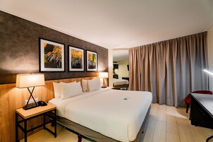 Quarto de hotel com uma cama grande, duas mesas de cabeceira com luminárias, uma escrivaninha e uma cadeira.
