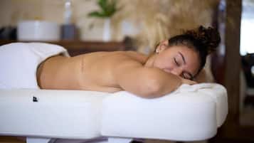A person lying on a massage table in a room with a plant and a white container in the background.