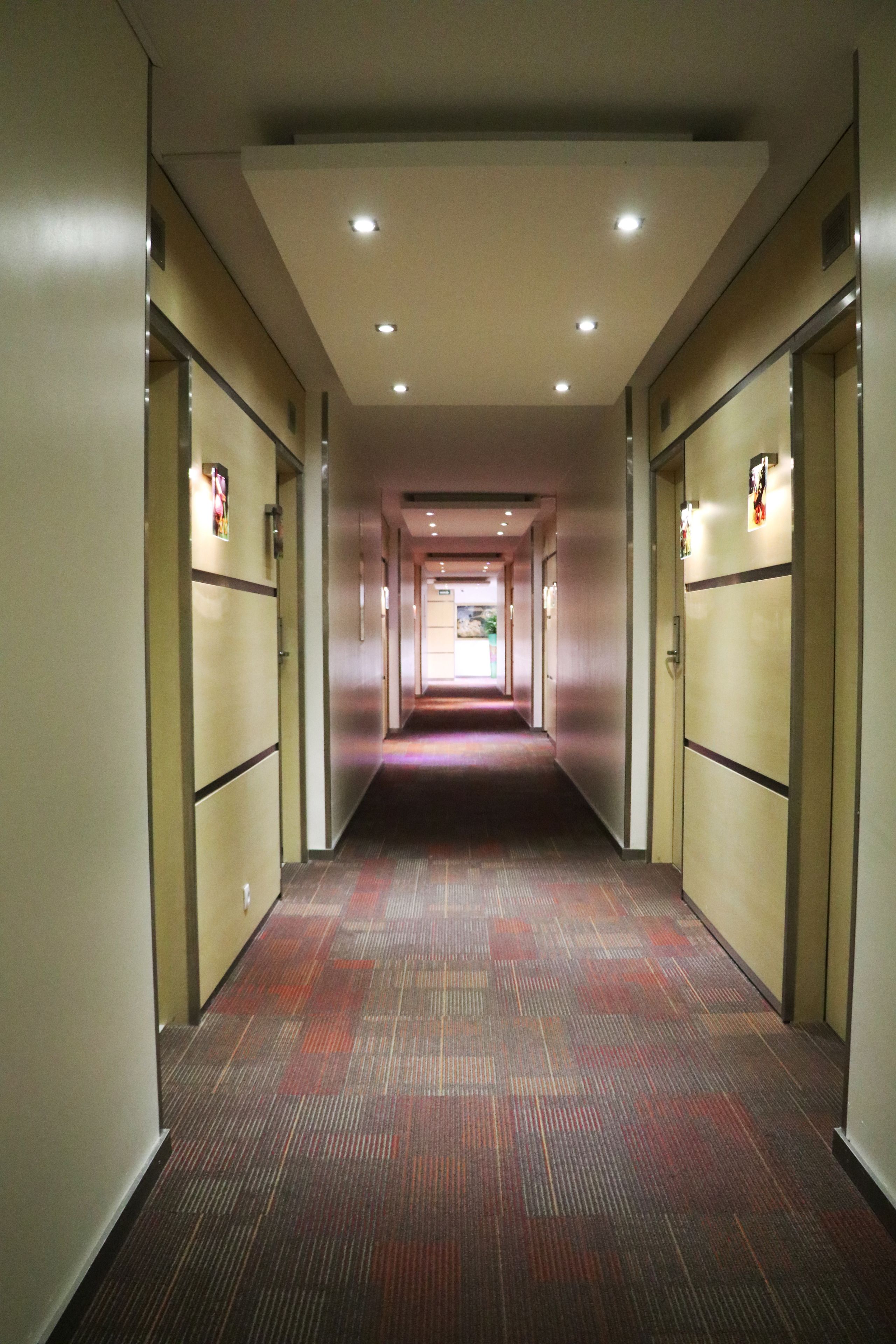 A hotel corridor with carpeted floors, doors on both sides, and recessed lighting on the ceiling.