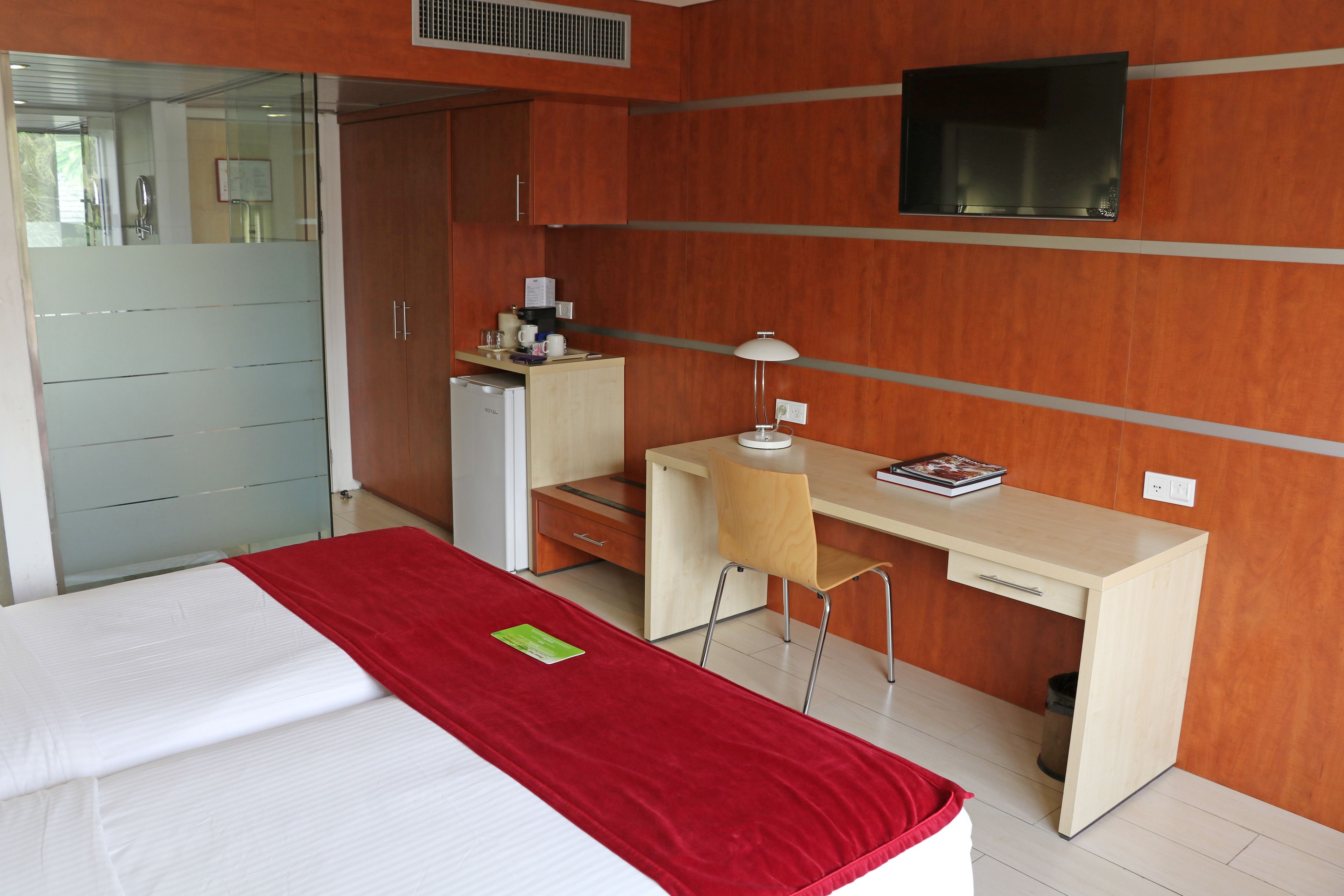 Habitació d'hotel amb un llit, una taula de treball, una cadira, un televisor i una cuineta petita.