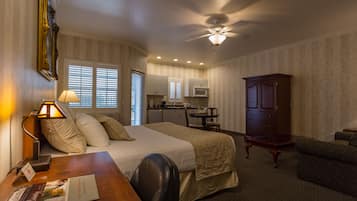 A hotel room with a bed, desk, chair, and a kitchenette area.