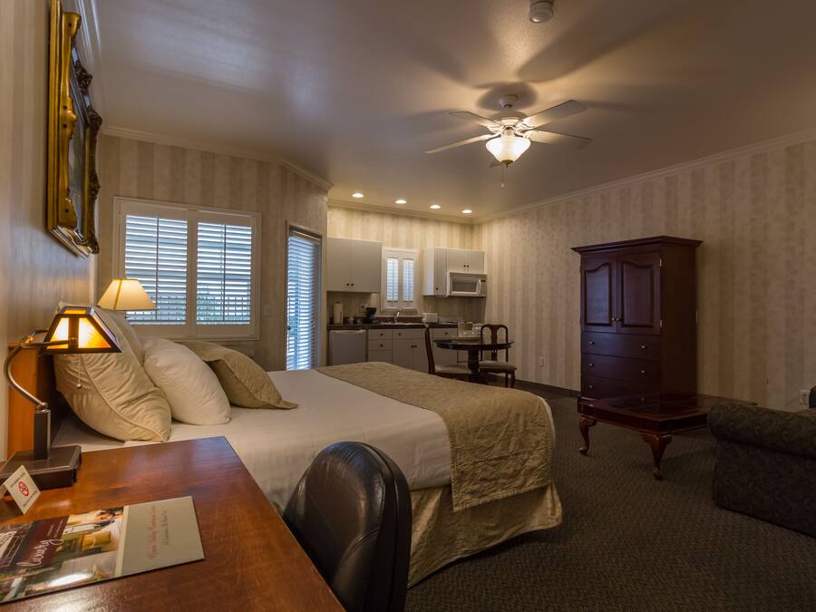 A hotel room with a bed, desk, chair, and a kitchenette area.