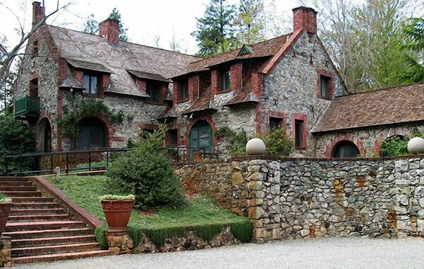 A stone building with a stone staircase leading to a green door, surrounded by a stone wall and potted plants.