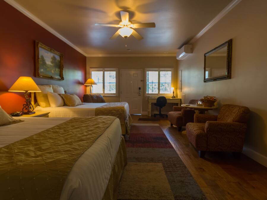 A hotel room with two beds, a desk, a chair, and a ceiling fan.