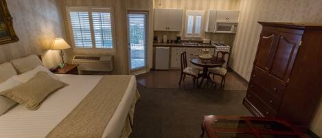 A hotel room with a bed, a desk, a chair, a dresser, a ceiling fan, and a kitchenette.
