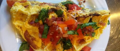 A plate with an omelette, tomatoes, and herbs.
