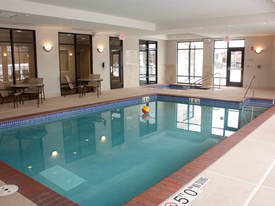 An indoor swimming pool with clear water, a lifeguard chair, and a poolside area with chairs and tables.
