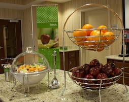 A buffet setup with a fruit bowl and a fruit basket on a granite countertop.