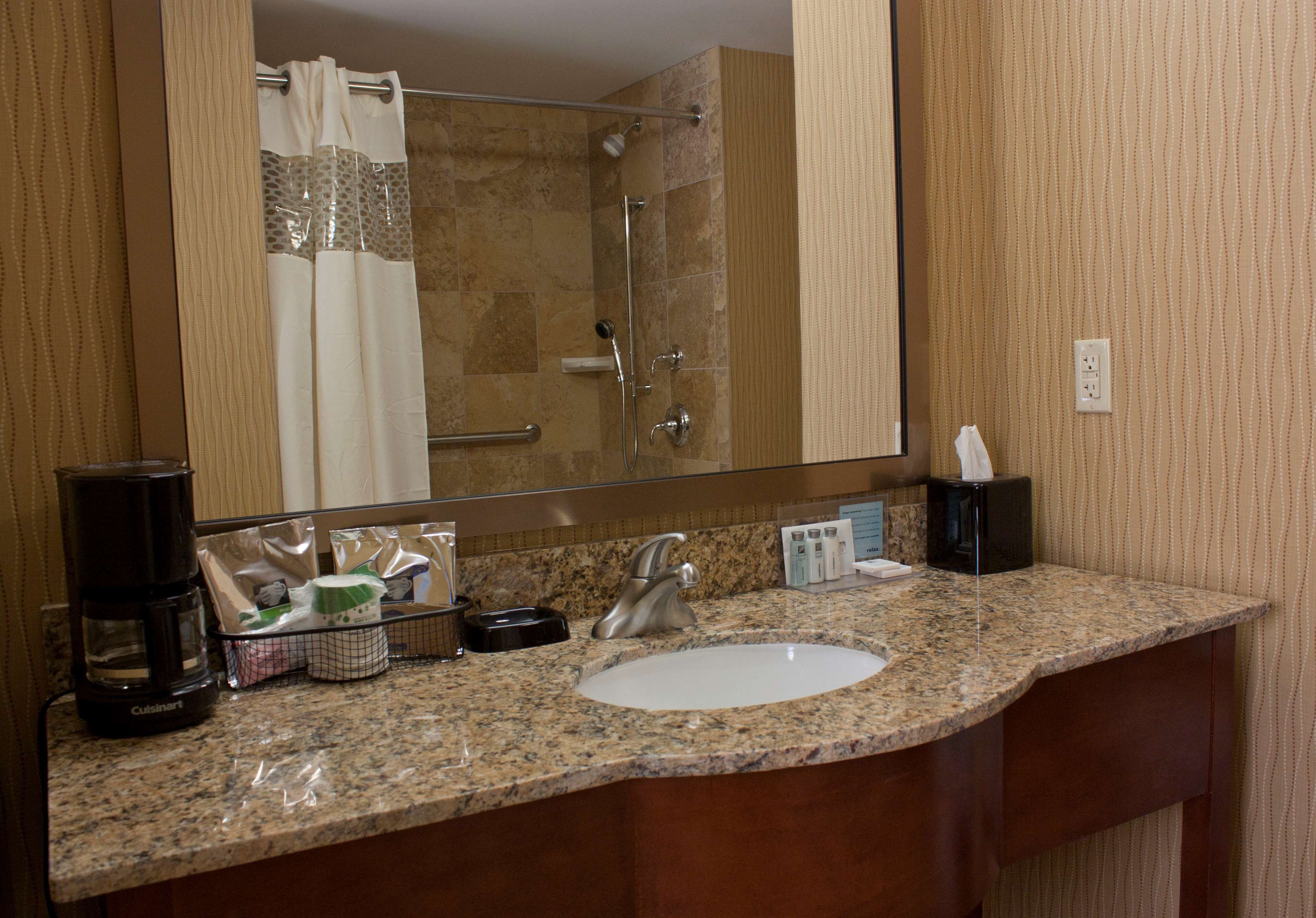 A bathroom with a granite countertop, a sink, a mirror, a shower, and toiletries.