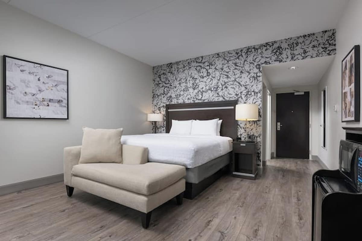 A hotel room with a bed, bedside lamps, a chair, a desk, and a microwave.
